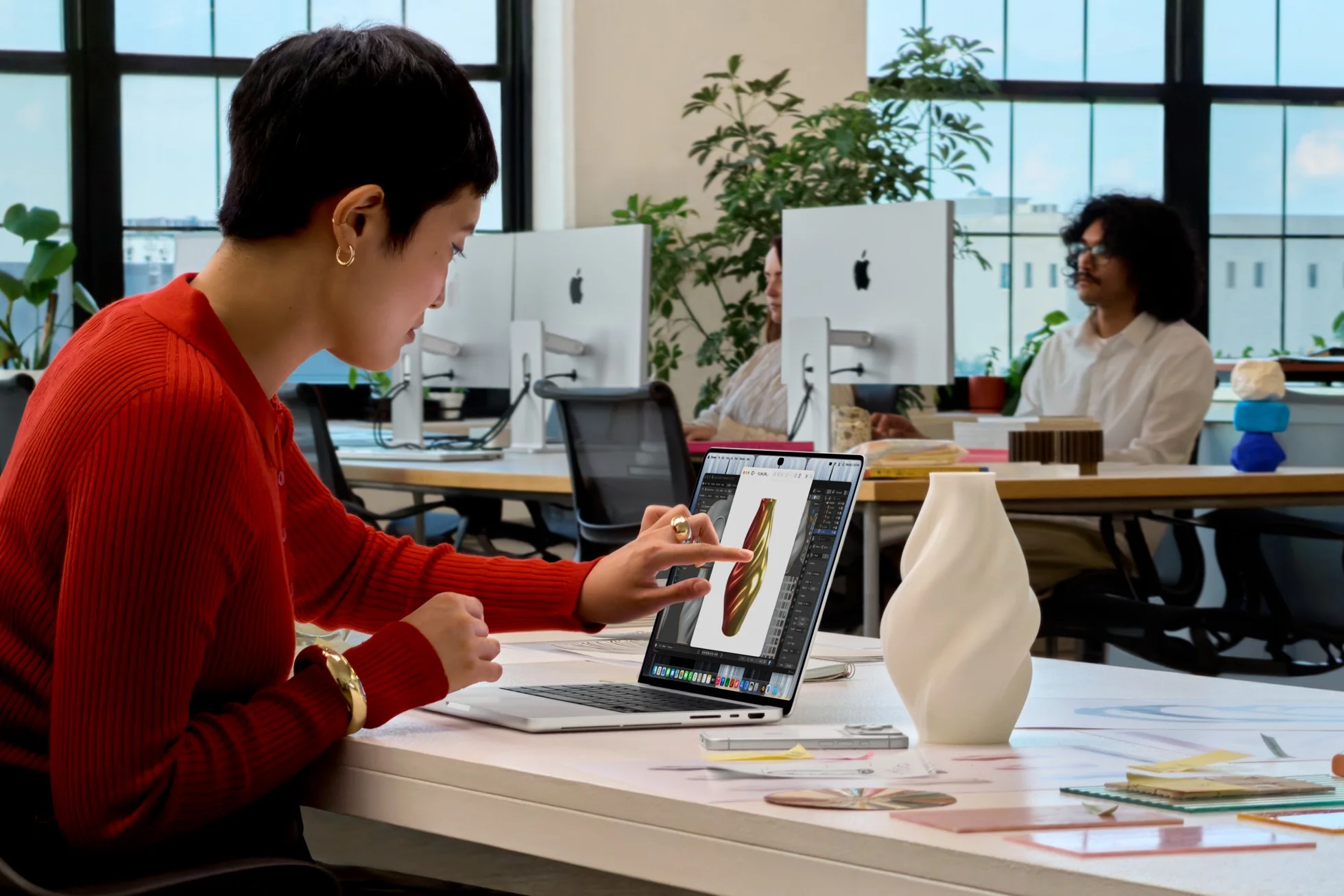 ผู้ใช้เสื้อแดงแตะหน้าจอ MacBook Pro ขณะทำงานออกแบบในออฟฟิศ